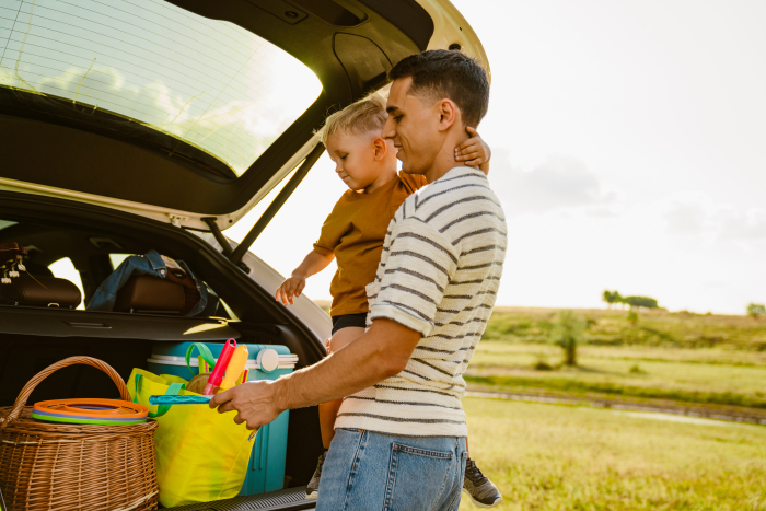 Pappa med barn lastar ut från bagage där bland annat en kylväska står. 